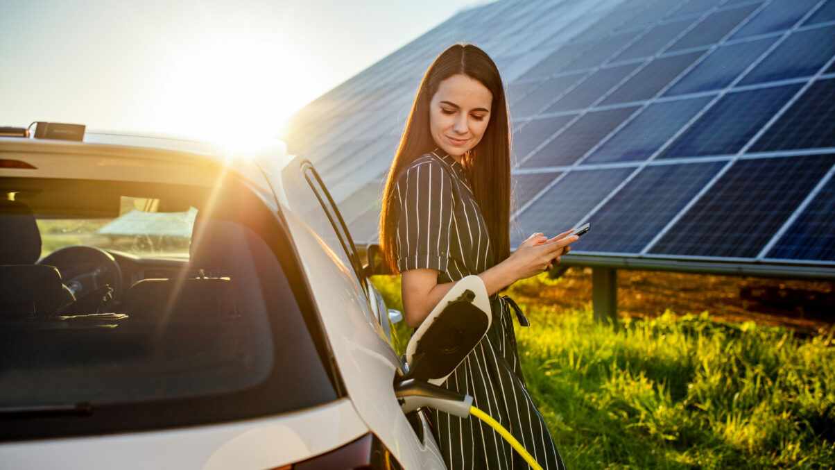 Frau wartet auf das Laden des e-Autos vor Photovoltaik-Anlage